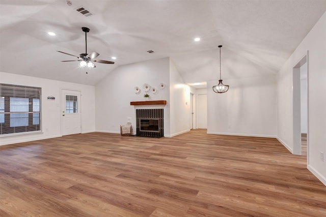 unfurnished living room featuring visible vents, lofted ceiling, a glass covered fireplace, ceiling fan with notable chandelier, and light wood-type flooring