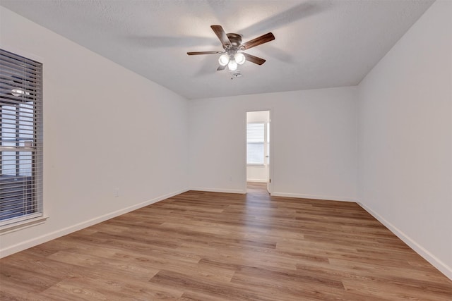 empty room with light wood-style flooring, a textured ceiling, baseboards, and a ceiling fan