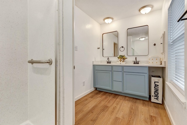 full bathroom featuring a sink, baseboards, wood finished floors, and double vanity