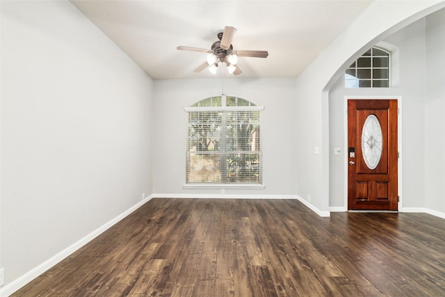 entryway featuring dark wood-type flooring, a ceiling fan, arched walkways, and baseboards