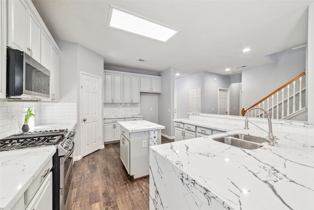 kitchen featuring a sink, light stone counters, decorative backsplash, appliances with stainless steel finishes, and dark wood-style flooring