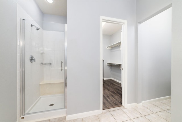 bathroom featuring a walk in closet, baseboards, a shower stall, and tile patterned flooring