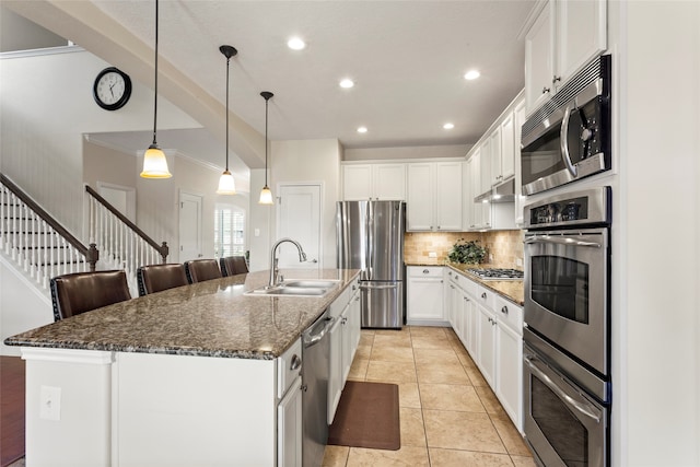 kitchen featuring a center island with sink, a sink, under cabinet range hood, appliances with stainless steel finishes, and decorative backsplash