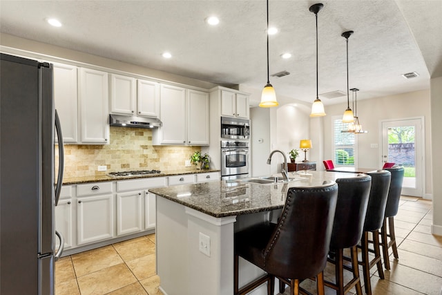 kitchen with visible vents, a sink, under cabinet range hood, appliances with stainless steel finishes, and tasteful backsplash