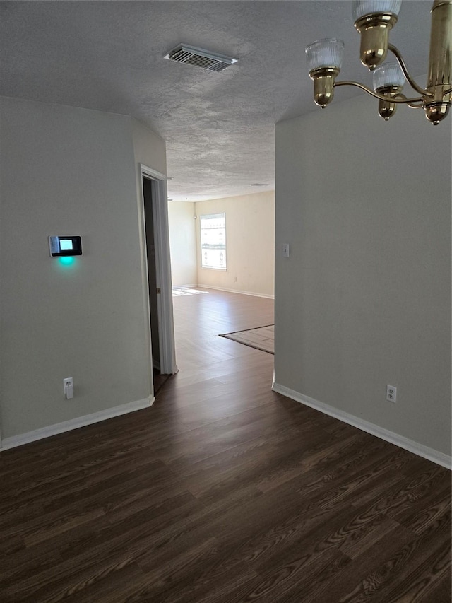 spare room with baseboards, a notable chandelier, dark wood finished floors, and visible vents