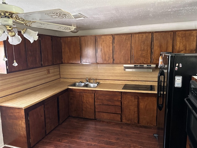 kitchen with under cabinet range hood, light countertops, dark wood-style floors, black appliances, and a sink