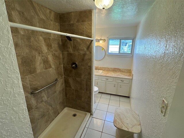 full bathroom featuring vanity, tiled shower, tile patterned flooring, a textured ceiling, and a textured wall