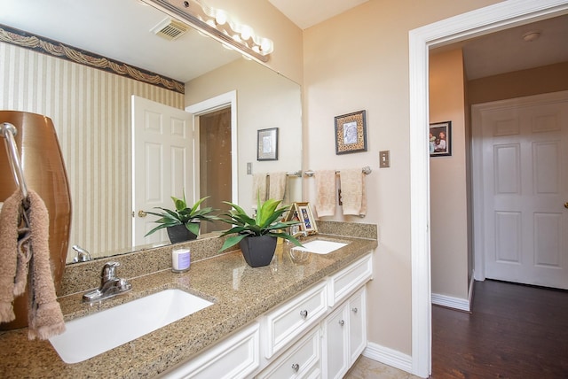 full bath featuring wood finished floors, visible vents, baseboards, double vanity, and a sink