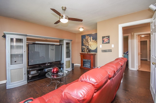 living area featuring a glass covered fireplace, baseboards, ceiling fan, and dark wood-style flooring