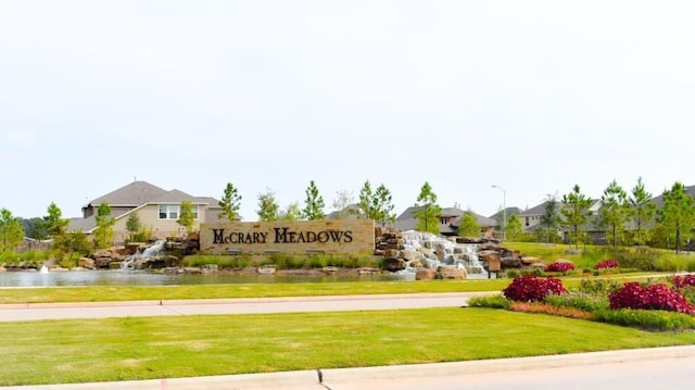 community sign featuring a residential view, a yard, and a water view