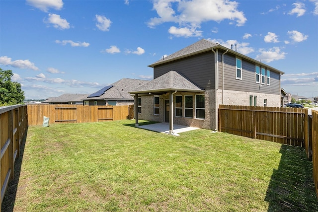 rear view of house featuring a yard, a patio, brick siding, and a fenced backyard