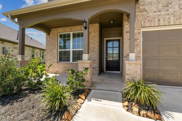 doorway to property with brick siding, a porch, and an attached garage