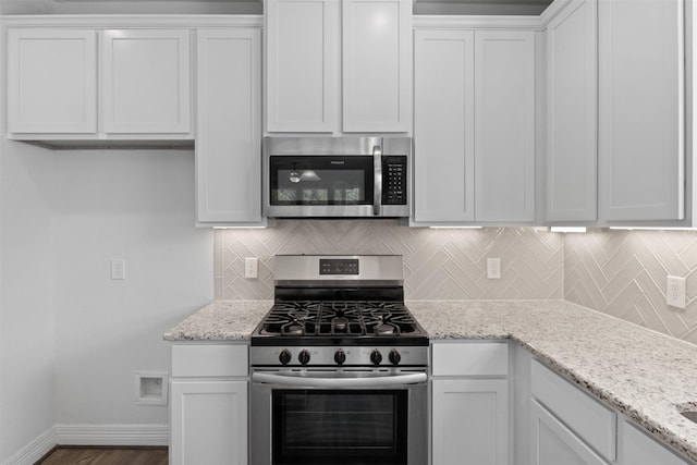 kitchen with light stone countertops, baseboards, stainless steel appliances, white cabinets, and tasteful backsplash