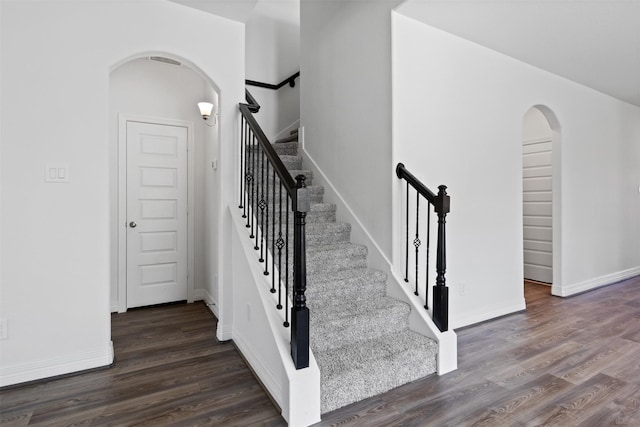 stairs featuring baseboards, arched walkways, and wood finished floors