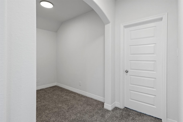 bonus room featuring lofted ceiling, arched walkways, dark colored carpet, and baseboards