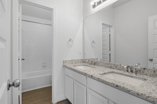 bathroom with double vanity, washtub / shower combination, wood finished floors, and a sink