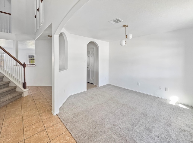 spare room featuring visible vents, stairway, light carpet, arched walkways, and light tile patterned flooring