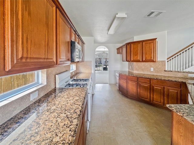 kitchen featuring light stone countertops, visible vents, white gas range oven, stainless steel microwave, and brown cabinets