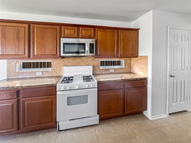 kitchen featuring stone countertops, stainless steel microwave, white range with gas cooktop, and brown cabinets