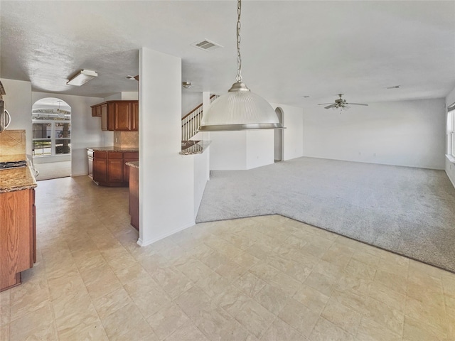 interior space featuring light floors, ceiling fan, open floor plan, light carpet, and brown cabinets