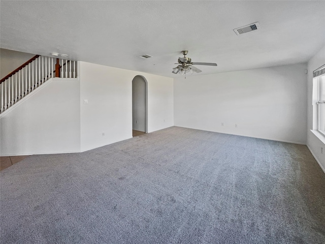 unfurnished room featuring stairway, visible vents, arched walkways, ceiling fan, and carpet flooring