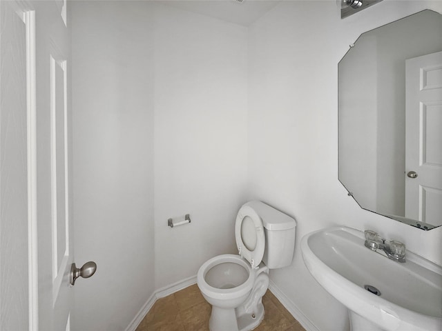 half bath with a sink, baseboards, toilet, and tile patterned flooring