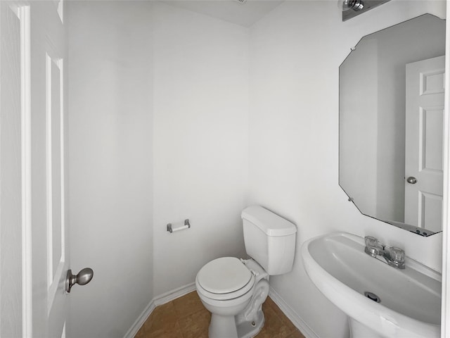 half bathroom featuring tile patterned flooring, toilet, baseboards, and a sink