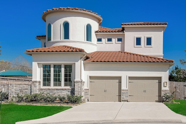 mediterranean / spanish home featuring fence, concrete driveway, a garage, stone siding, and a tiled roof