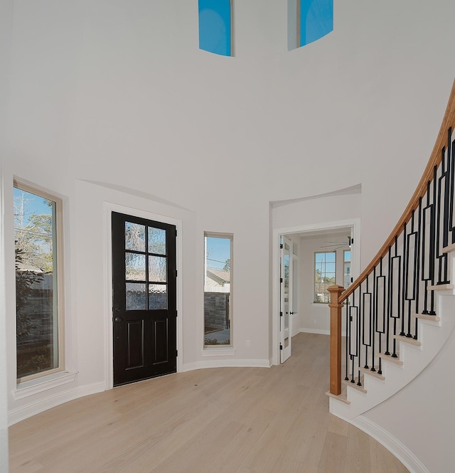 entrance foyer with light wood finished floors, baseboards, stairs, and a towering ceiling