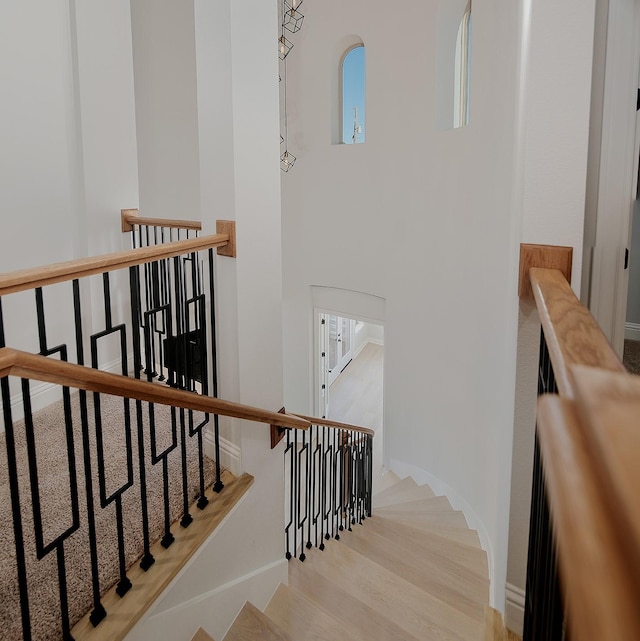 stairs featuring baseboards, wood finished floors, and a towering ceiling