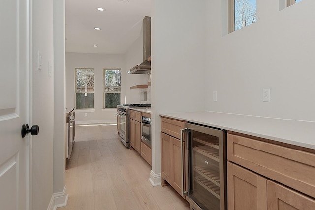 kitchen featuring recessed lighting, wine cooler, appliances with stainless steel finishes, wall chimney exhaust hood, and light wood finished floors