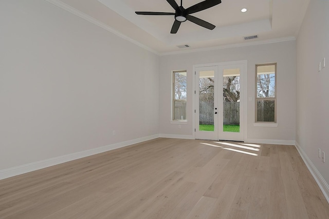 empty room featuring a wealth of natural light, light wood-style flooring, baseboards, and a tray ceiling