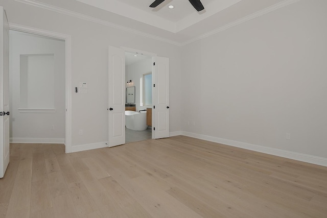 unfurnished bedroom with a tray ceiling, baseboards, light wood-style flooring, and crown molding