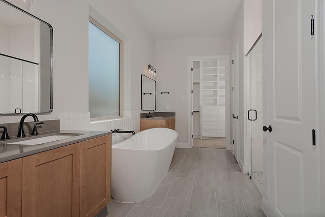 full bath with a walk in closet, two vanities, a stall shower, a sink, and a freestanding bath