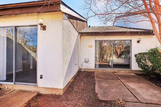 exterior space featuring stucco siding, a patio, and roof with shingles