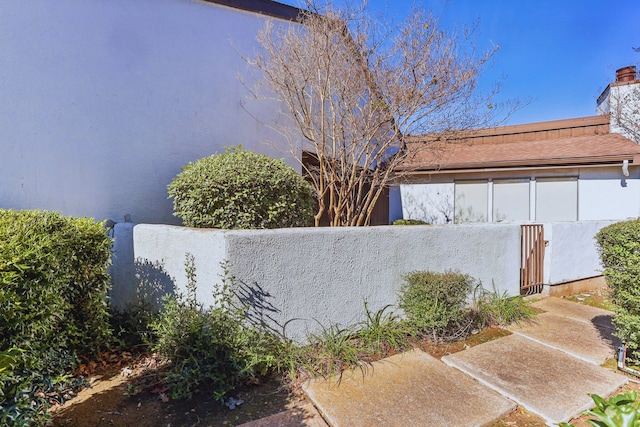 view of side of home featuring a fenced front yard, stucco siding, and a chimney