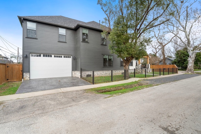 view of front facade featuring a fenced front yard, an attached garage, a shingled roof, and aphalt driveway