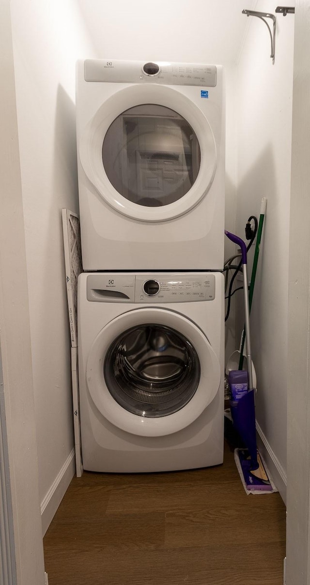 clothes washing area featuring laundry area, stacked washing maching and dryer, baseboards, and wood finished floors