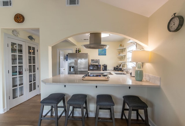 kitchen with visible vents, stainless steel refrigerator with ice dispenser, a sink, a peninsula, and island range hood