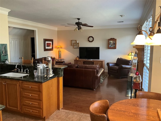 kitchen featuring ornamental molding, a ceiling fan, a sink, dark countertops, and brown cabinetry