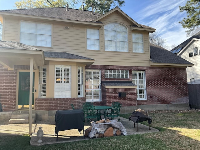 back of property featuring brick siding, roof with shingles, and a patio area