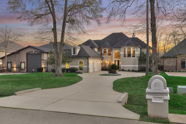 french country inspired facade featuring curved driveway, a front lawn, a garage, and stucco siding