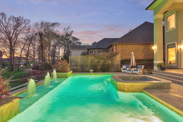 pool at dusk with a pool with connected hot tub and fence