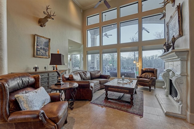 living room with light tile patterned flooring, a fireplace with raised hearth, crown molding, and a ceiling fan