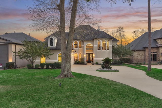 french country style house featuring stucco siding, a lawn, curved driveway, french doors, and a chimney