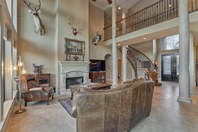 tiled living room with a fireplace with raised hearth, baseboards, stairs, decorative columns, and a towering ceiling