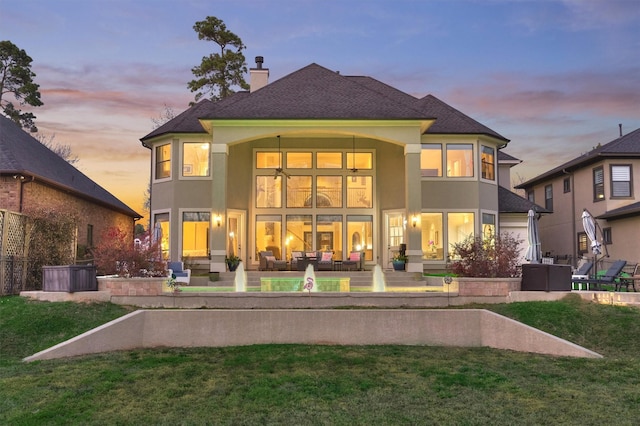 back of property at dusk with an outdoor living space, a chimney, a lawn, and a patio