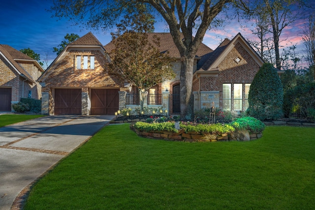 english style home with driveway, a yard, a garage, stone siding, and brick siding