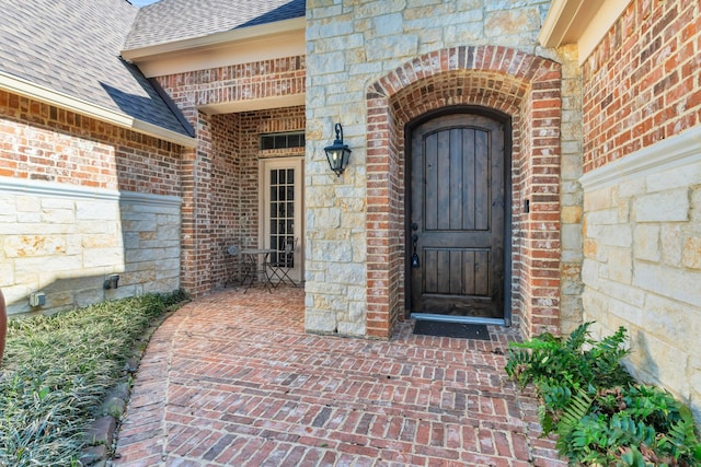 doorway to property featuring stone siding, brick siding, and roof with shingles