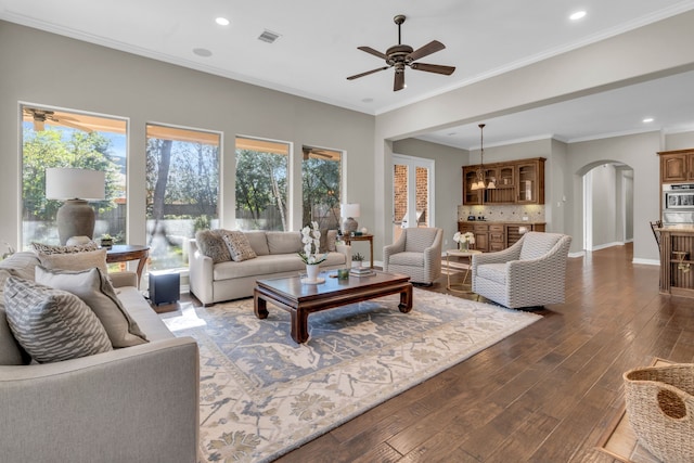 living area with crown molding, baseboards, dark wood-style floors, arched walkways, and a ceiling fan